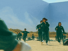 a group of people in green uniforms are running on a sandy field .