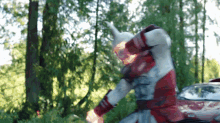a man in a red and white costume with horns is standing in a forest