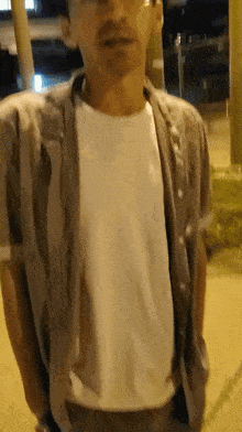 a man wearing glasses and a white shirt stands on a sidewalk at night