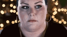 a woman wearing hoop earrings and a necklace is making a funny face .