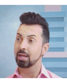 a man with a beard and mustache is wearing a pink shirt and making a funny face .