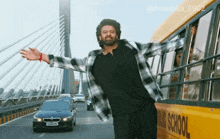 a man in a plaid shirt is standing next to a school bus
