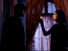 a man and a woman are standing next to each other in front of a window .