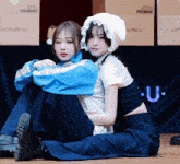 two girls sit next to each other in front of boxes that say with mu u.