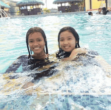 two girls are swimming in a pool and smiling