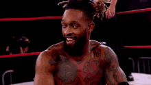 a wrestler with tattoos on his chest is sticking his tongue out in a wrestling ring .
