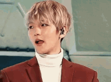 a young man wearing a red suit and a white turtleneck is making a surprised face .