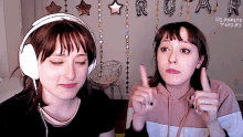 two girls wearing headphones are giving a thumbs up