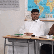 a man in a white shirt sits at a desk in front of a world map