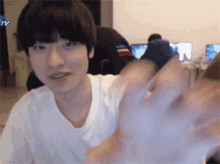 a young man in a white t-shirt is waving his hand at the camera .