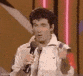 a man in a white jacket is holding a microphone and making a funny face .