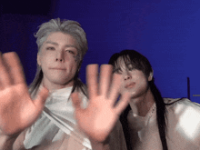 a man with long hair and a tattoo on his face stands next to another man with their hands up