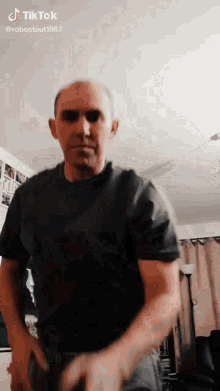 a man wearing sunglasses and a black shirt is dancing in a living room with tiktok written on the bottom