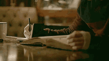 a person is writing in a notebook with a pen while sitting at a table .