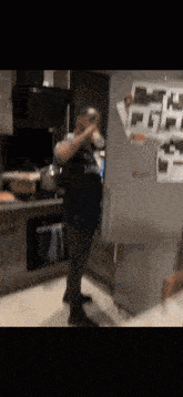 a man in a blue shirt is drinking from a cup while standing in front of a refrigerator