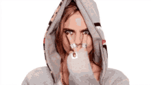 a woman wearing a hoodie and rings is covering her face with her hand .