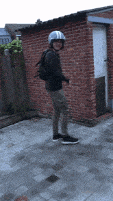 a man wearing a helmet and a backpack stands in front of a brick building