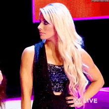 a blonde woman in a black dress is standing on a stage with her hands on her hips .