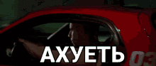 a man is driving a red car with the word axuetb written on the window