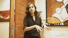 a woman in a black shirt is standing in front of a painting that says made in animotica
