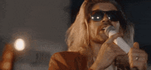 a man with long hair is singing into a microphone while wearing sunglasses .