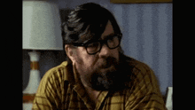 a man with glasses and a beard is sitting in front of a lamp in a room .