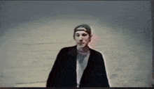 a man wearing a baseball cap and a black jacket is standing in a dark room