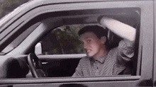a man is sitting in the driver 's seat of a car with his arm out the window .