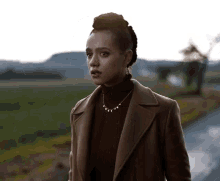 a woman wearing a brown coat and a turtleneck is standing on a road .