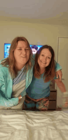 two women are posing for a picture on a bed