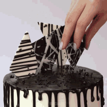 a woman 's hand is reaching for a piece of chocolate on top of a black and white cake