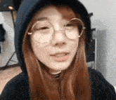a woman wearing glasses and a hoodie is looking at the camera .