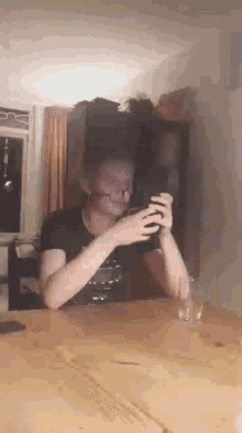 a man is sitting at a table taking a picture of himself with a cell phone .