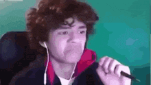a young man with curly hair is wearing headphones and crying while smoking a cigarette .