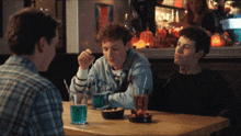 three men are sitting at a table with drinks and snacks and one of the drinks says ' coca cola ' on it