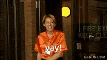 a woman in an orange shirt is standing in front of a fire exit