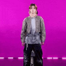 a man wearing a jacket and tie dye shirt stands in front of a purple background