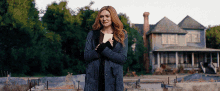 a woman in a coat is standing in front of a house holding a piece of paper .