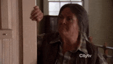 a woman in a plaid shirt is standing in a doorway and looking out .
