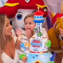 a woman is standing next to a child holding a cake with paw patrol characters on it .
