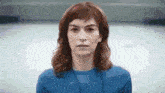 a woman with red hair and a blue shirt is looking at the camera .
