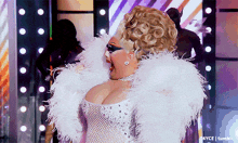 a woman in a white dress with feathers on her shoulders is on a stage