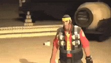 a man wearing a yellow headband and a vest is standing in front of a large object .