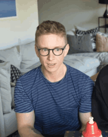 a man wearing glasses and a blue striped shirt sits in front of a couch