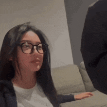 a woman wearing glasses is sitting on a couch looking at a man .