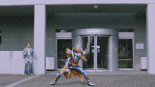 a man in a superhero costume stands in front of a building with a woman standing behind him