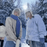 two men are standing in the snow wearing sweaters and scarves .