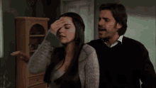 a man and a woman are standing next to each other and the woman is holding her head