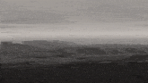 a black and white photo of a landscape with mountains and a river