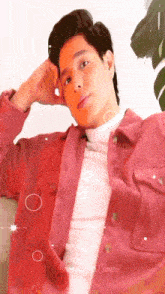 a man in a pink jacket and white turtleneck is sitting on a couch with his hands on his head .